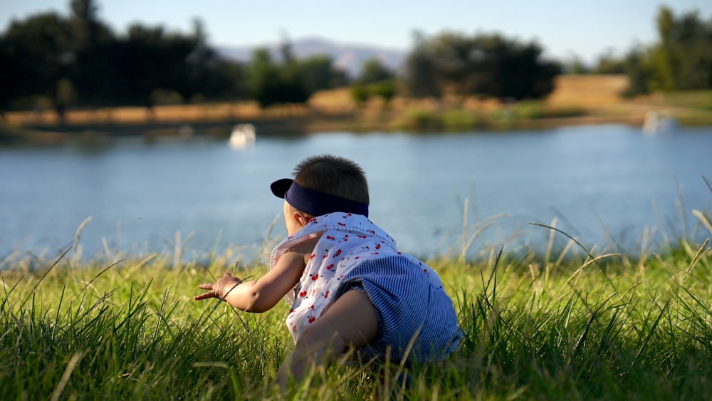 girl in blue and white stripe shirt sitting on green grass field near lake during daytime
