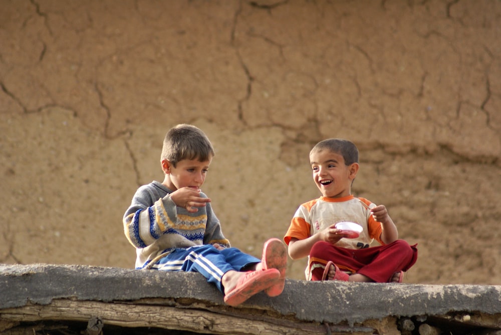 2 boys sitting on brown concrete bench during daytime