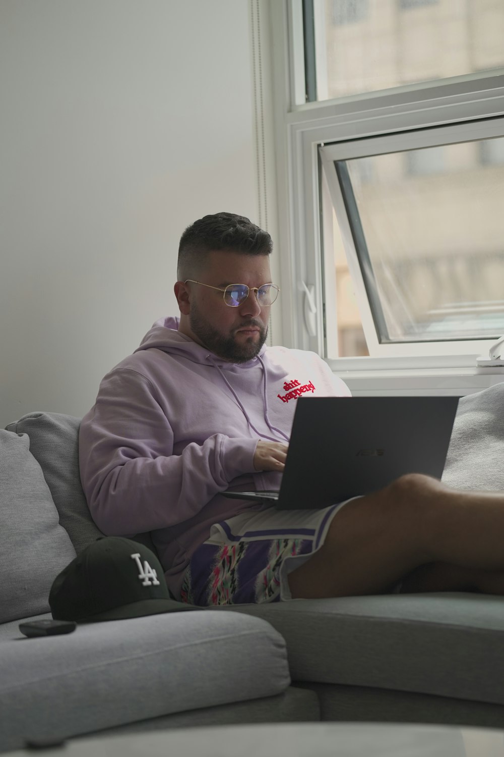 man in pink dress shirt wearing black sunglasses sitting on gray couch