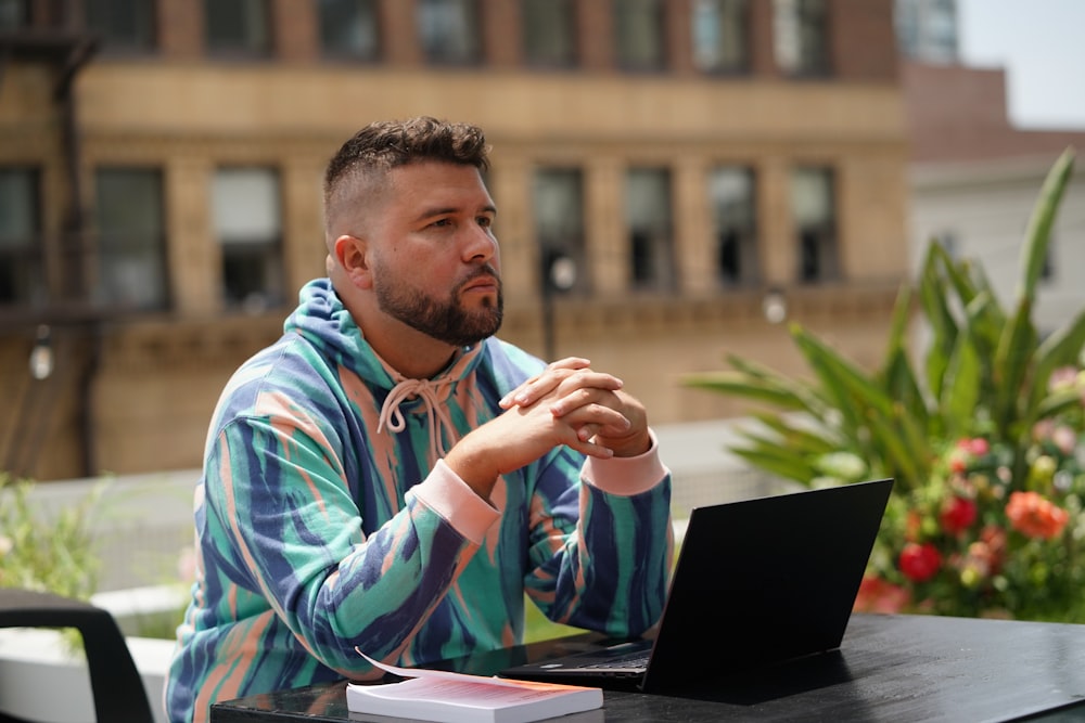 man in blue and white tribal print hoodie sitting beside black laptop computer