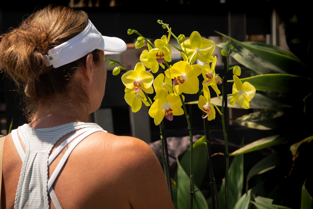 woman in white tank top wearing white sunglasses standing beside yellow flower