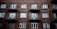 A brick apartment building facade with several windows and balconies. The structure appears aged but sturdy, with simple metallic railings on each balcony. The overall architectural style is utilitarian.
