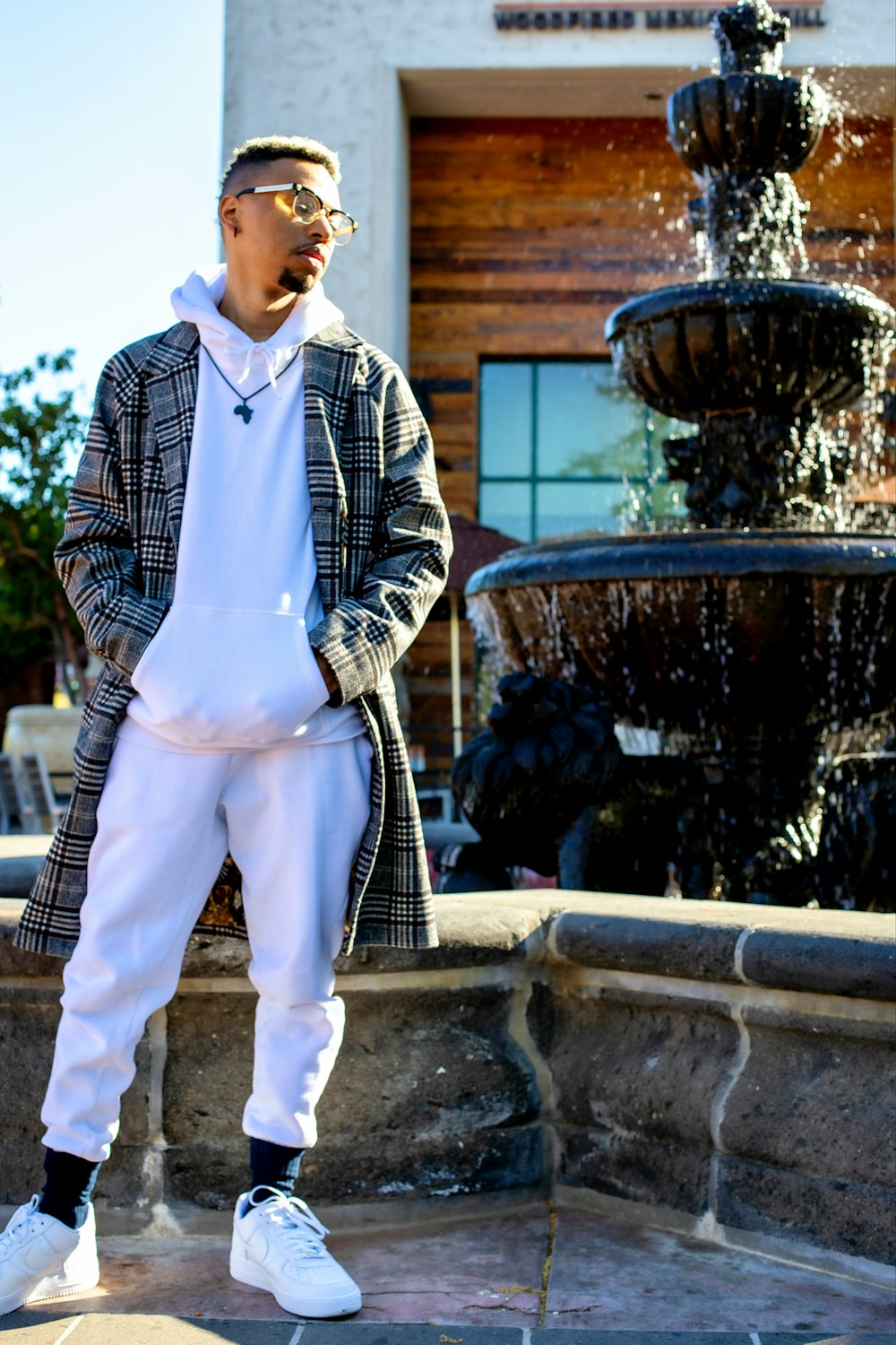 man in blue and white striped dress shirt and white pants standing near fountain during daytime
