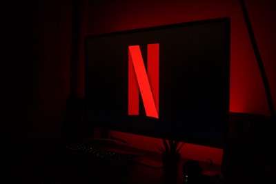A computer monitor displays a large red 'N' central on a black screen, surrounded by a dark room with a dim red glow. A keyboard and small plant sit below the monitor.
