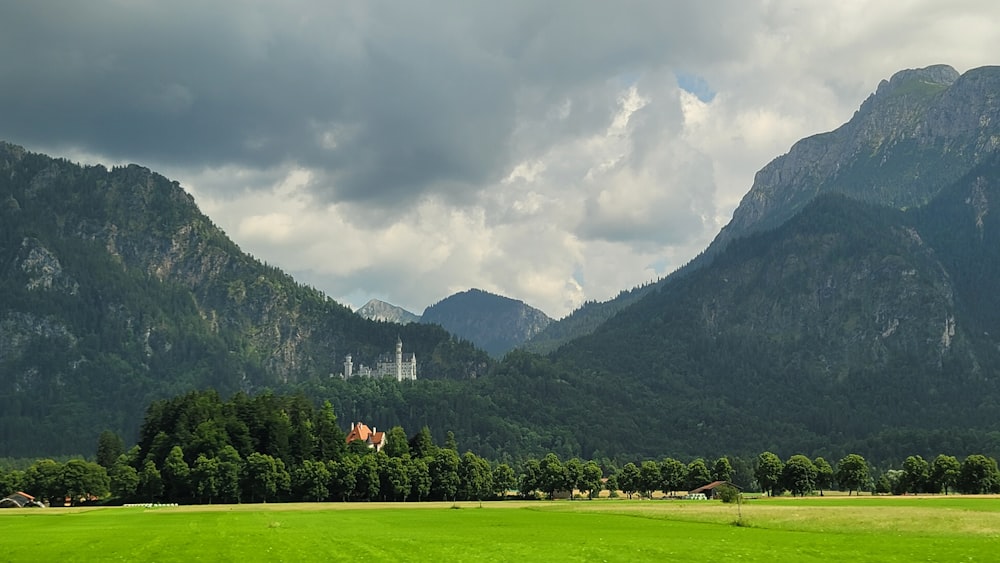 green grass field near mountain under cloudy sky during daytime