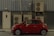 A compact red car is parked beside a building with multiple air conditioning units mounted on a corrugated metal wall. A small door with a rectangular window is visible on the left side of the image.