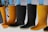 A row of rubber boots, primarily in black and yellow colors, are hanging upside down. The background features a few green leaves and a plain, light backdrop.