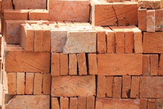 A stack of red-orange bricks with rough textures and visible cracks, arranged in an orderly manner.