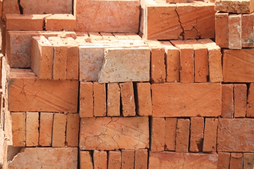 A stack of red-orange bricks with rough textures and visible cracks, arranged in an orderly manner.