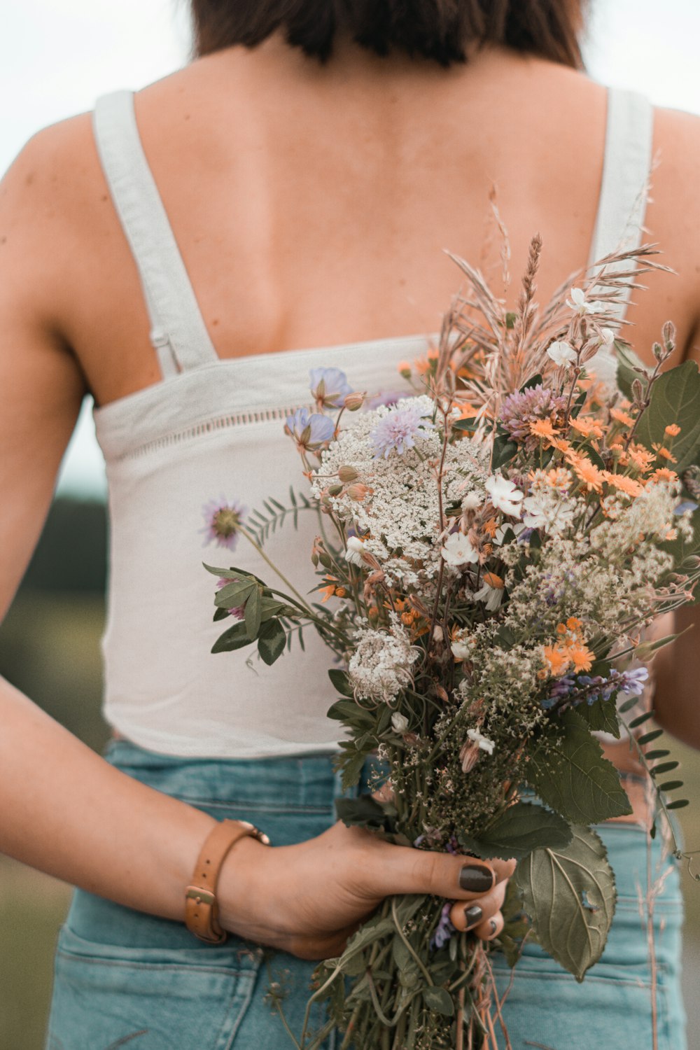 woman in white tank top holding bouquet of flowers