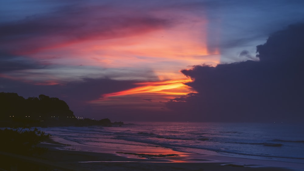 silhouette of mountain near body of water during sunset