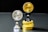 Two coins labeled 'EXU' are standing upright on holders. One is silver and placed on a silver stand, the other is gold and placed on a stack of gold coins. The coins feature leaf designs.