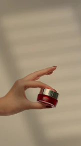 Close-up of diverse hands holding éclat rose cream jars with gold lids against a soft pink background.