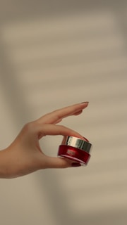 An elegant hand holding a small jar of nourishing cream.