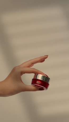 An elegant hand holding a small jar of nourishing cream.