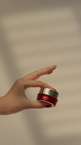 Close-up of diverse hands holding éclat rose cream jars with gold lids against a soft pink background.