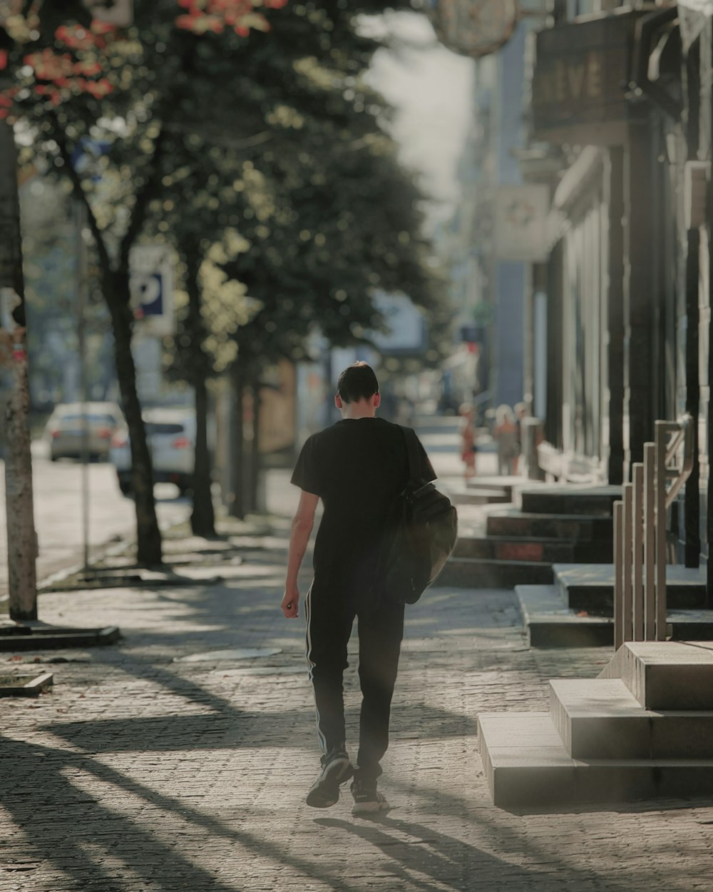 man in black hoodie walking on sidewalk during daytime