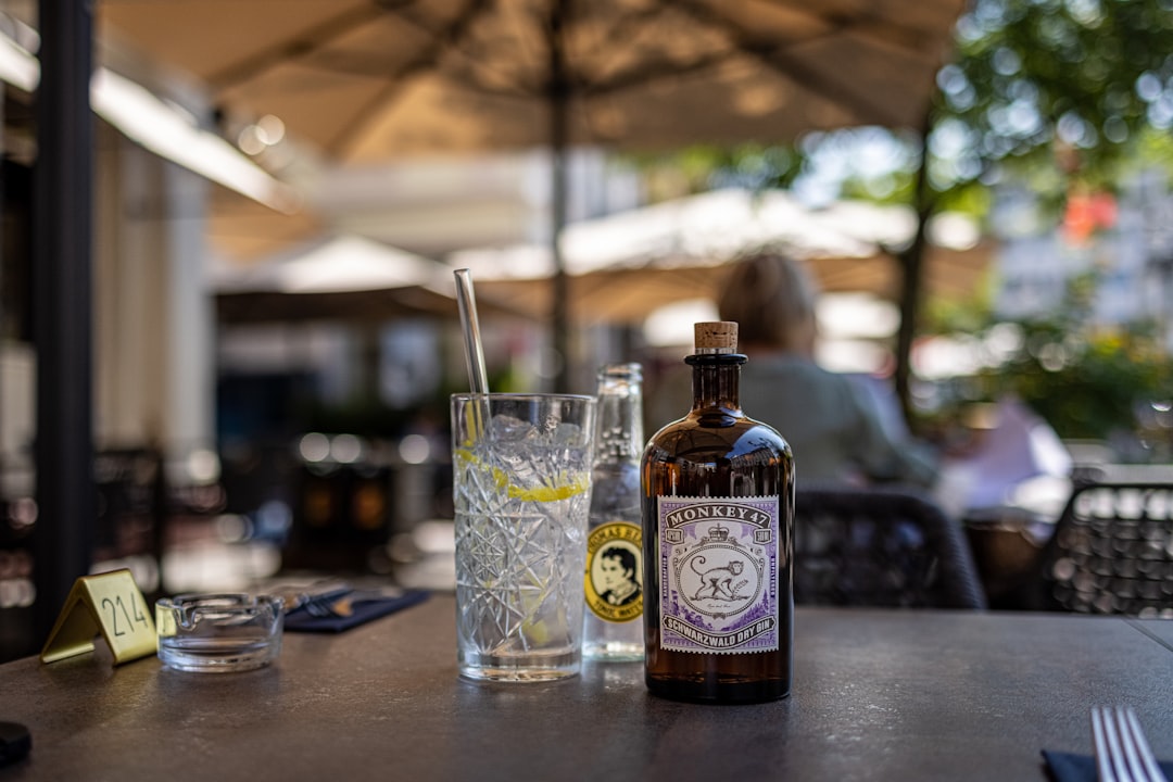 clear drinking glass beside brown glass bottle on brown wooden table