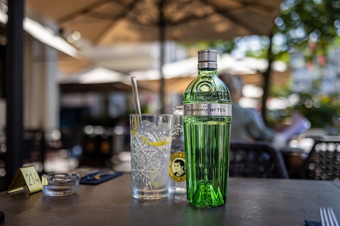 clear drinking glass beside green glass bottle on table
