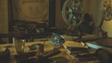 A dimly lit room with vintage film projectors and reels set on a cluttered wooden table. There are stacks of paperwork and several small objects, including a glass, scattered across the surface. An old tapestry with decorative text hangs on the wall, adding to the nostalgic atmosphere.