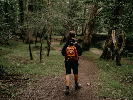 man in black and red jacket walking on dirt road