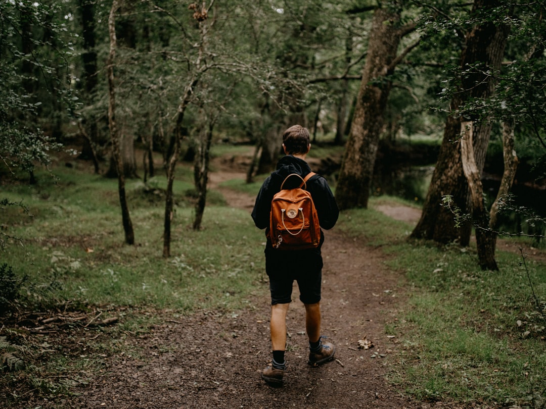 man in black and red jacket walking on dirt road