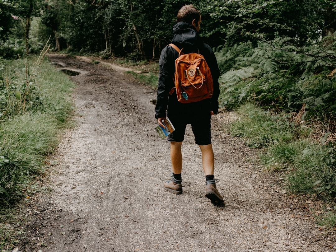 man in black and orange backpack walking on dirt road during daytime