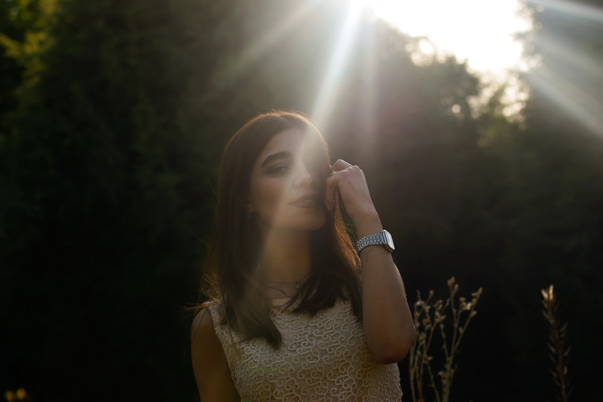 A model wearing a flowing, earth-toned boho dress standing in a sunlit natural setting with greenery.