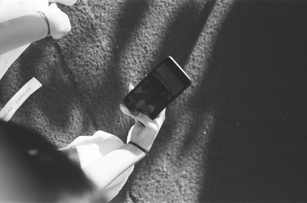 person in white long sleeve shirt holding black smartphone