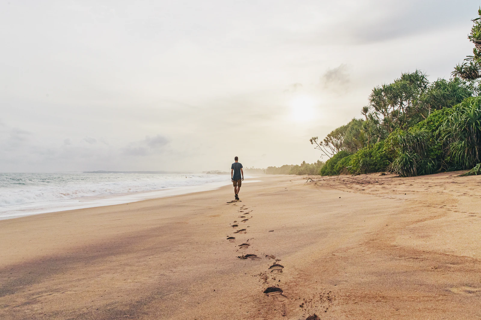 Travel photograph: A lone person walks beside footprints on a broad, less busy Tangalle beach.