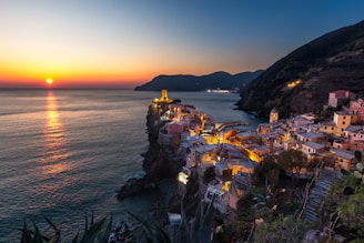 A cinematic sunset over a serene coastal village, with warm golden light reflecting on the water and lush greenery surrounding charming architecture.