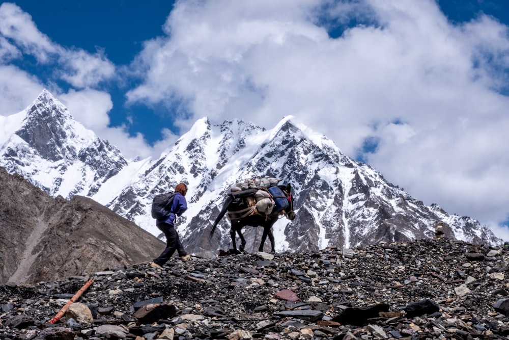 man in black jacket and blue denim jeans standing on rocky mountain under white clouds and