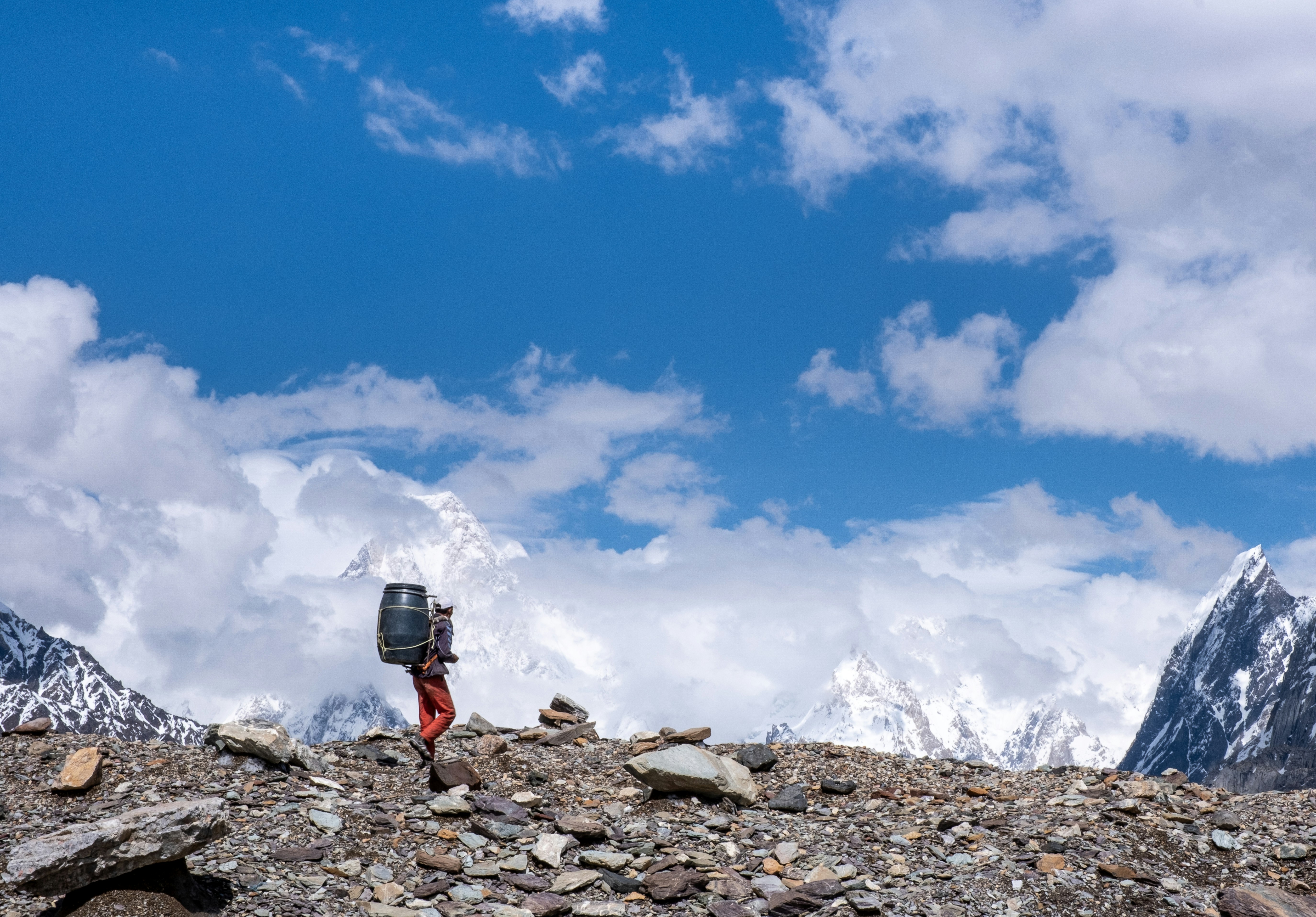 黒のジャケットと青のデニムジーンズを着た人が、青と白の下の岩場に立っている