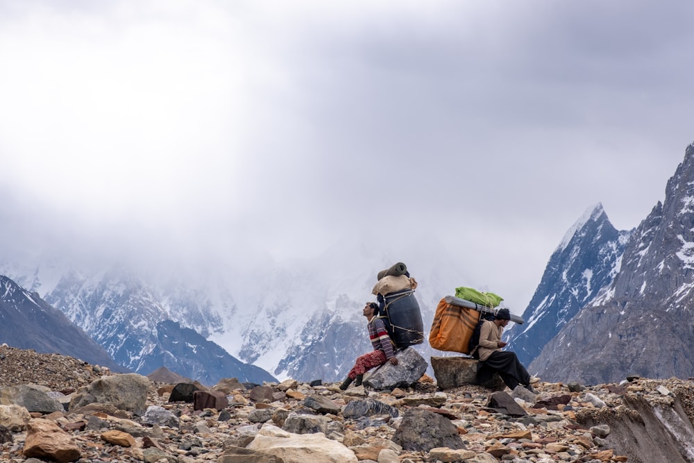 homme en veste verte et sac à dos noir debout sur un sol rocheux regardant une montagne enneigée