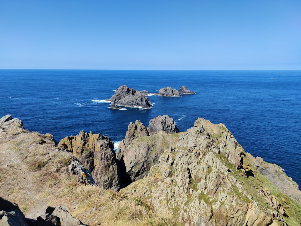 green and gray rock formation beside blue sea under blue sky during daytime