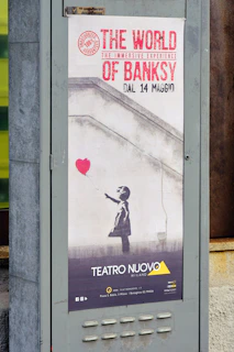 A vibrant street gallery wall featuring a famous Banksy stencil of a girl releasing a heart-shaped balloon.