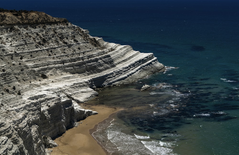 montanha rochosa branca ao lado do mar azul durante o dia