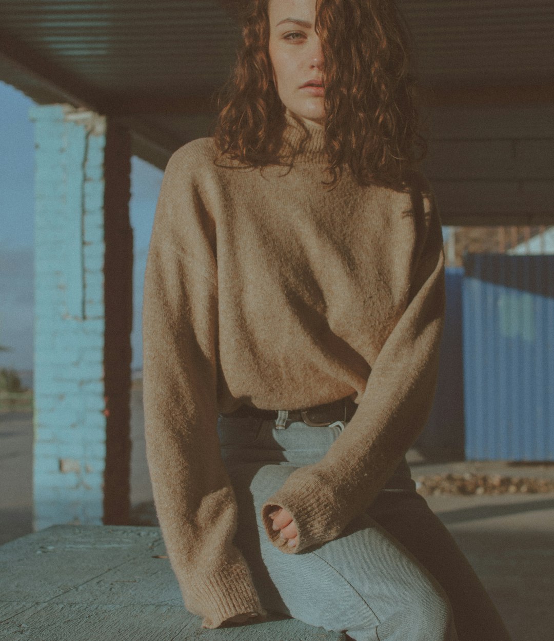 woman in brown sweater and gray leggings sitting on gray concrete floor