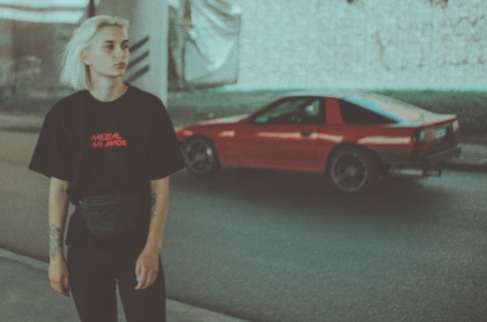 man in black crew neck t-shirt standing beside red car