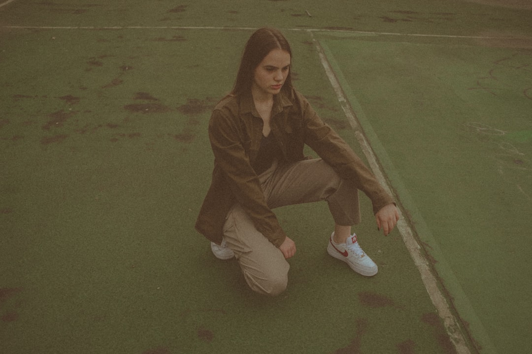 woman in brown jacket and white pants sitting on green floor