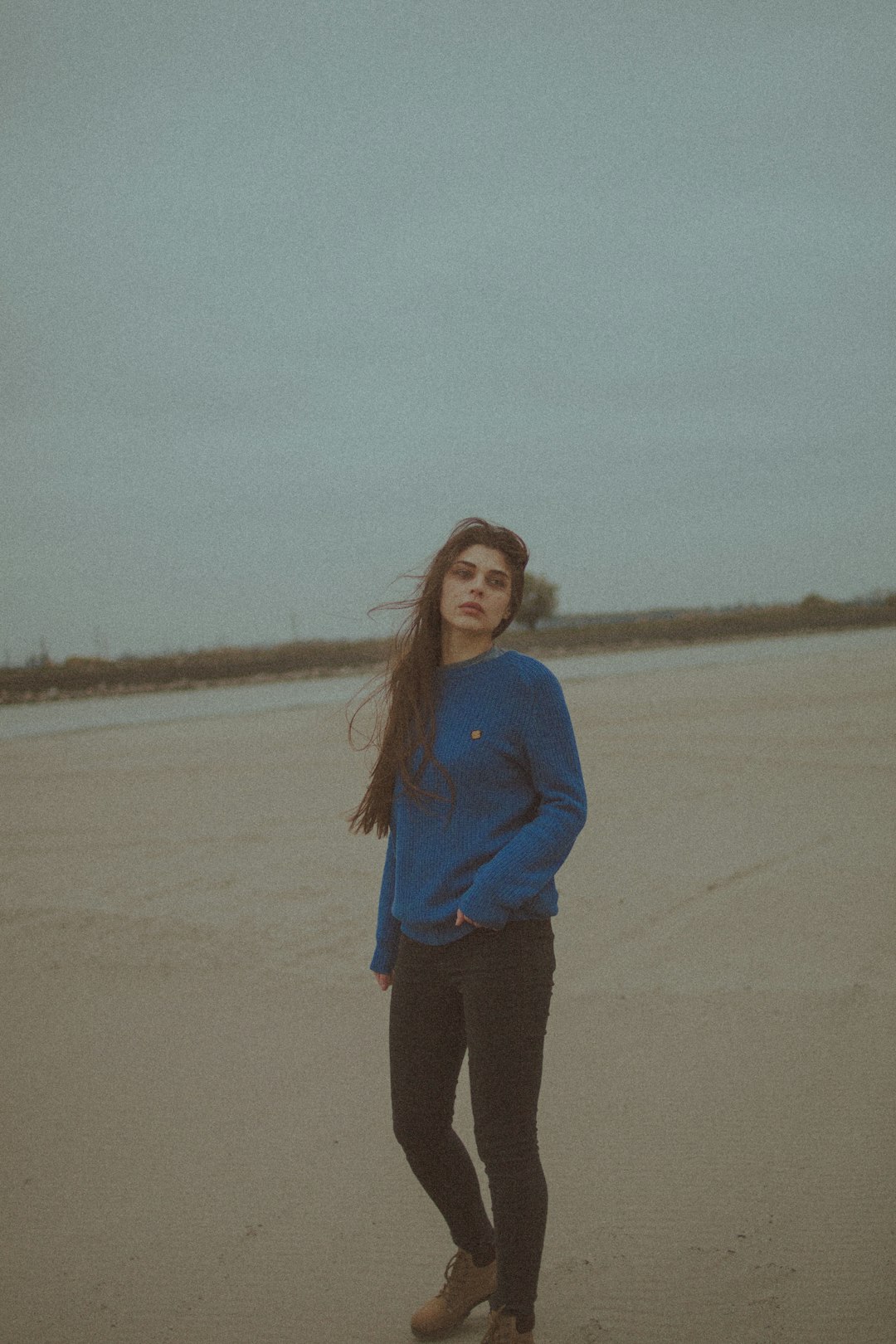 woman in blue long sleeve shirt standing on brown sand during daytime