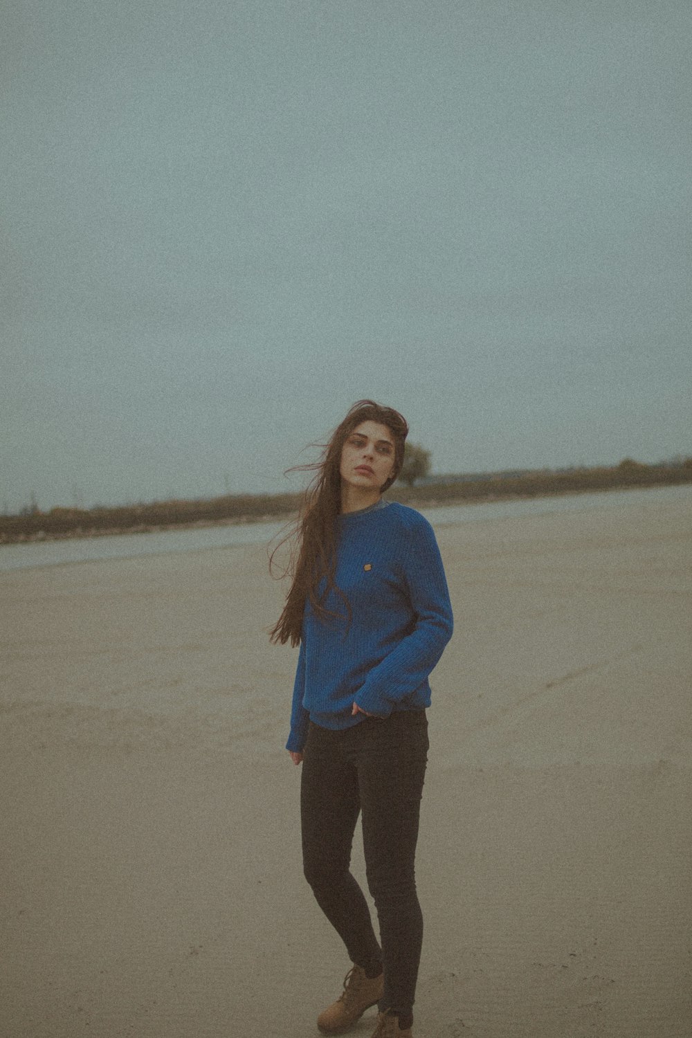 Femme en chemise à manches longues bleue debout sur le sable brun pendant la journée