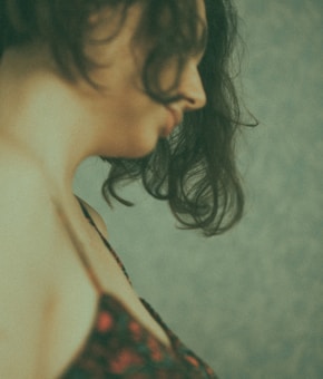 A side profile of a person with dark, wavy hair against a textured, muted background. The image has a soft, grainy effect, creating an artistic and introspective atmosphere.
