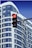 A modern building with blue and white curved architectural design is in the background. In the foreground, there is a traffic light displaying a red signal. A security camera is mounted on the traffic light pole.