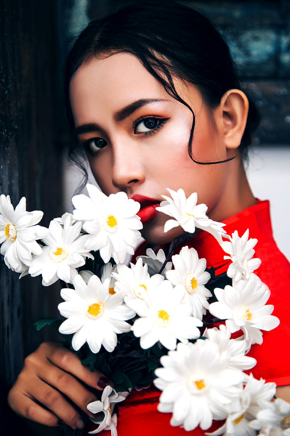 白いデイジーの花を持つ赤いシャツの女性