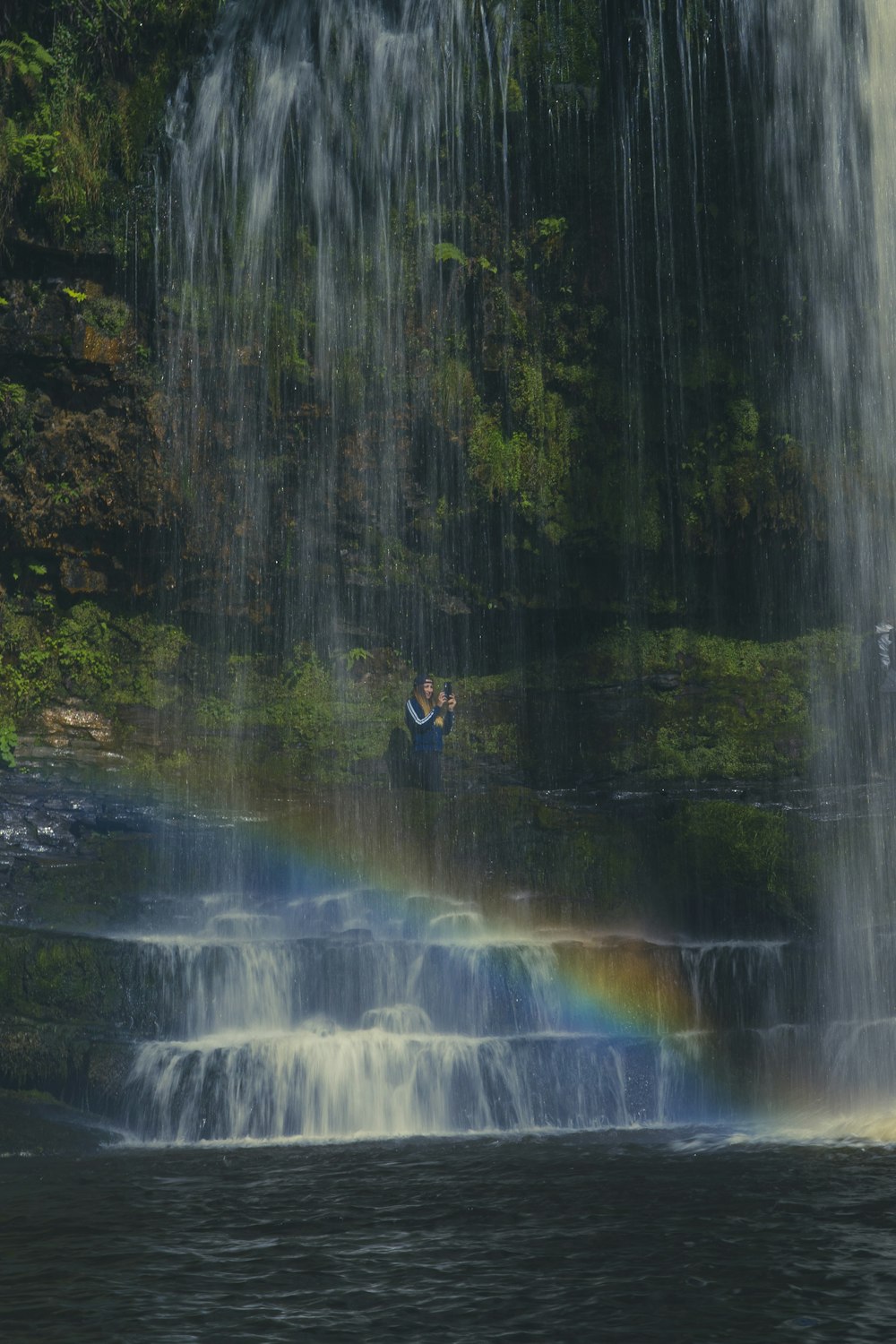 man in black jacket sitting on rock in front of waterfalls during daytime