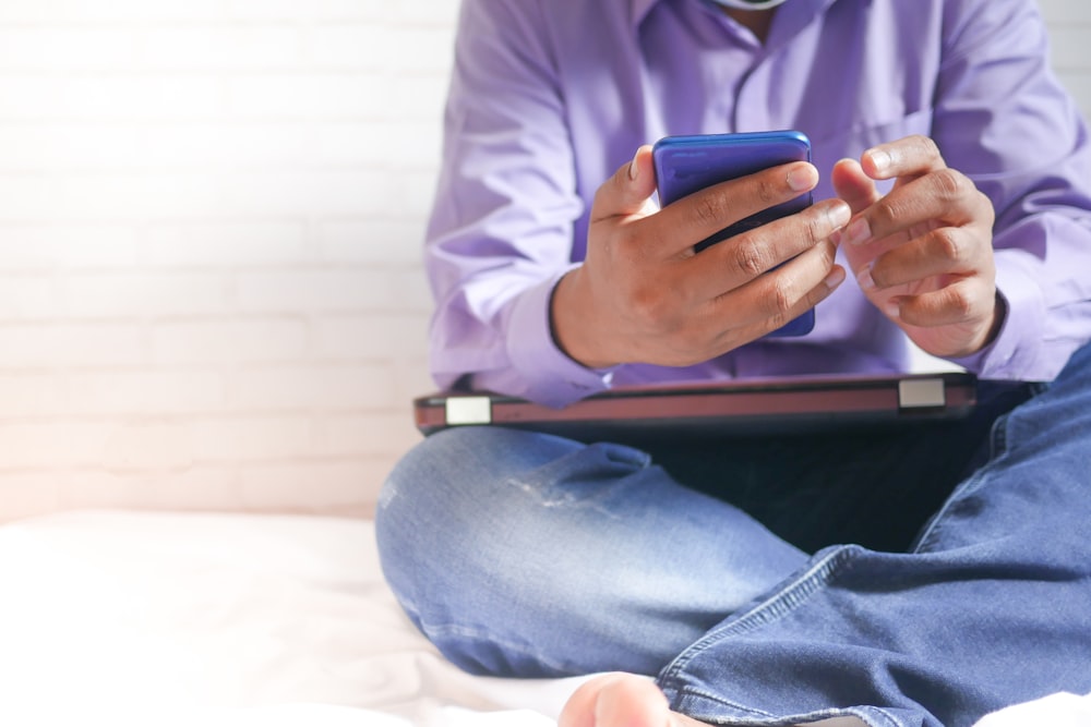 man in white dress shirt and blue denim jeans sitting on bed