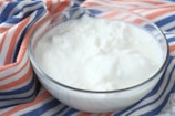 A bowl filled with creamy white yogurt is placed on a fabric with orange, blue, and white stripes.