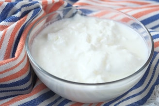 A bowl filled with creamy white yogurt is placed on a fabric with orange, blue, and white stripes.