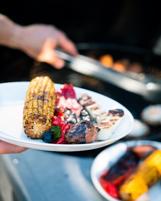 person holding stainless steel fork with grilled meat on white ceramic plate